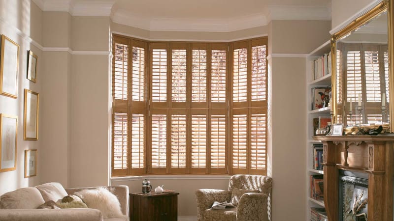 Light brown wood tier on tier shutters on a bay window in a living room